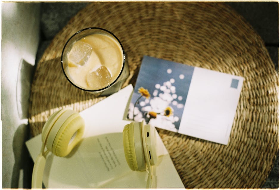 A relaxing setup featuring iced coffee, headphones, and a postcard on a wicker surface.