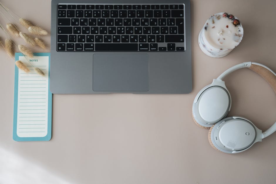 A top view of a minimalist desk setup featuring a laptop, headphones, and a notepad.